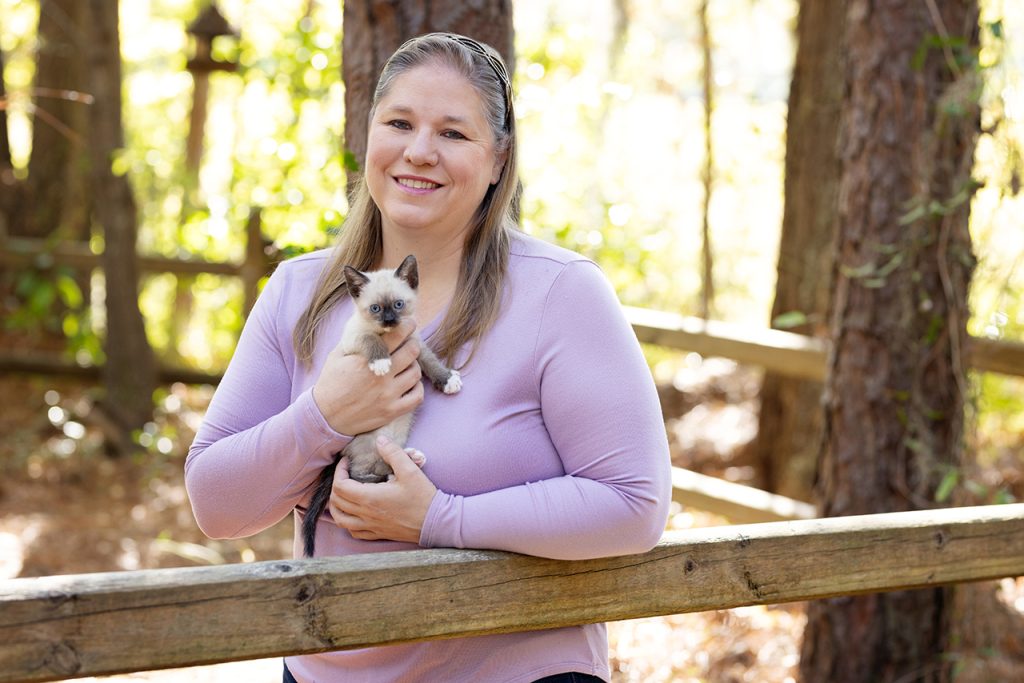 Blonde woman standing outside and holding a siamese kitten