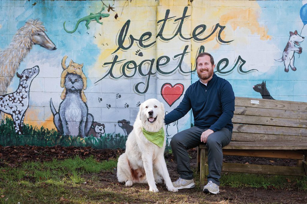 Bearded man sitting on a bench with his hand on the shoulder of a big fluffy white dog