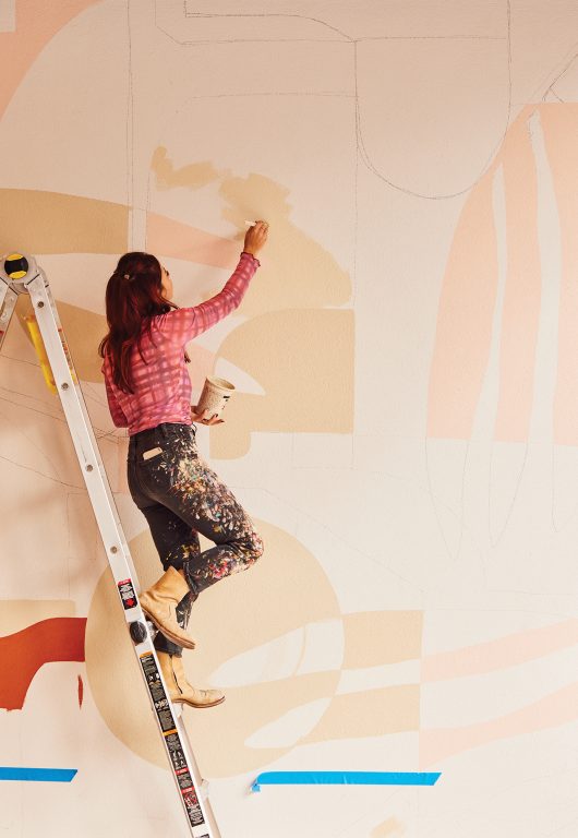 Artist JULU standing on a ladder, painting a mural inside Hotel Bardo