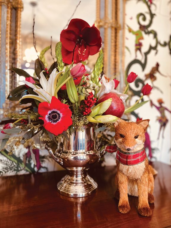 Fox statue next to a silver vase full of red flowers