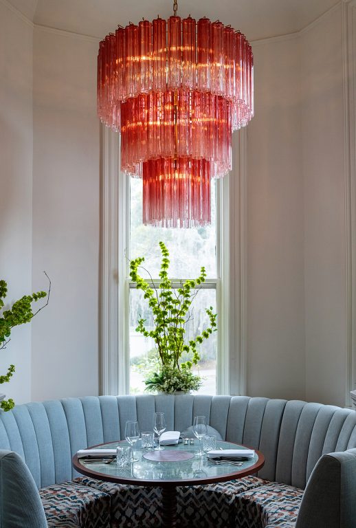 A pink crystal chandelier hangs over a small round dining table and round upholstered booth