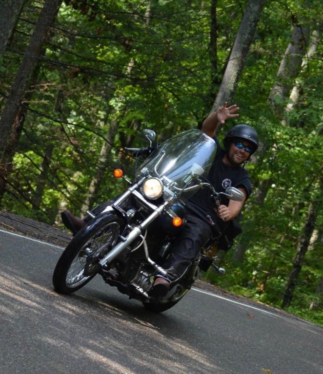 man riding a motorcycle on a tree-lined road