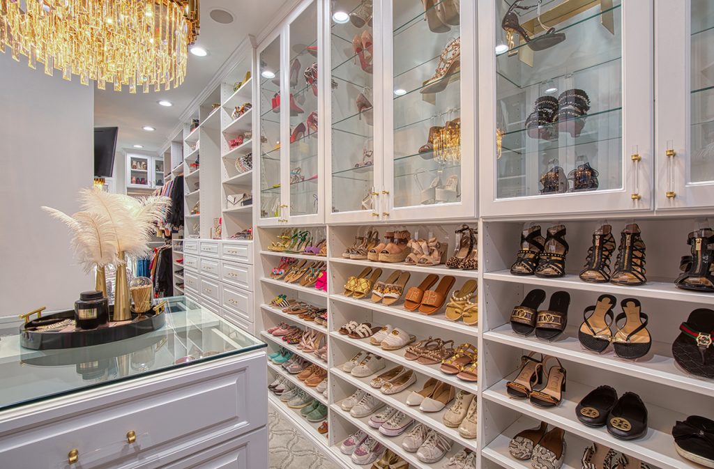 Huge bedroom closet with rows upon rows of women's shoes on shelves and behind glass cabinet doors