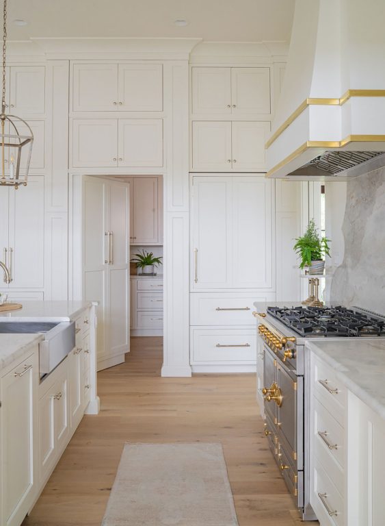 Designer kitchen with light natural wood floors and white floor-to-ceiling cabinets