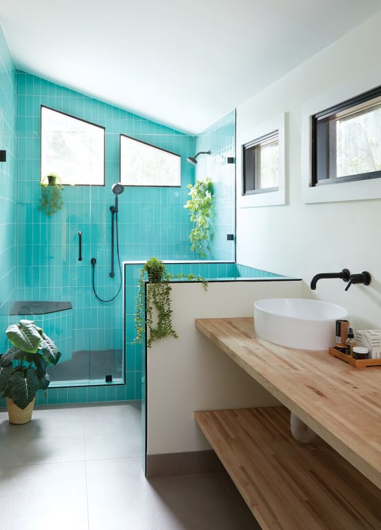 Modern bathroom with aqua colored vertical subway shower tiles, black hardware and natural wood sinktop