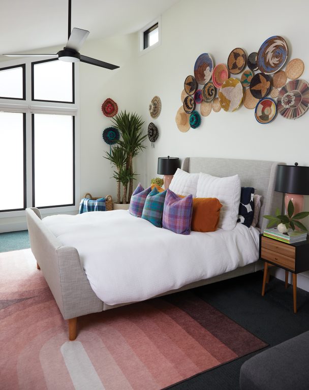 Primary bedroom with colorful pillows, a rug in shades of red and woven hats and bowls hanging on the wall in a collage