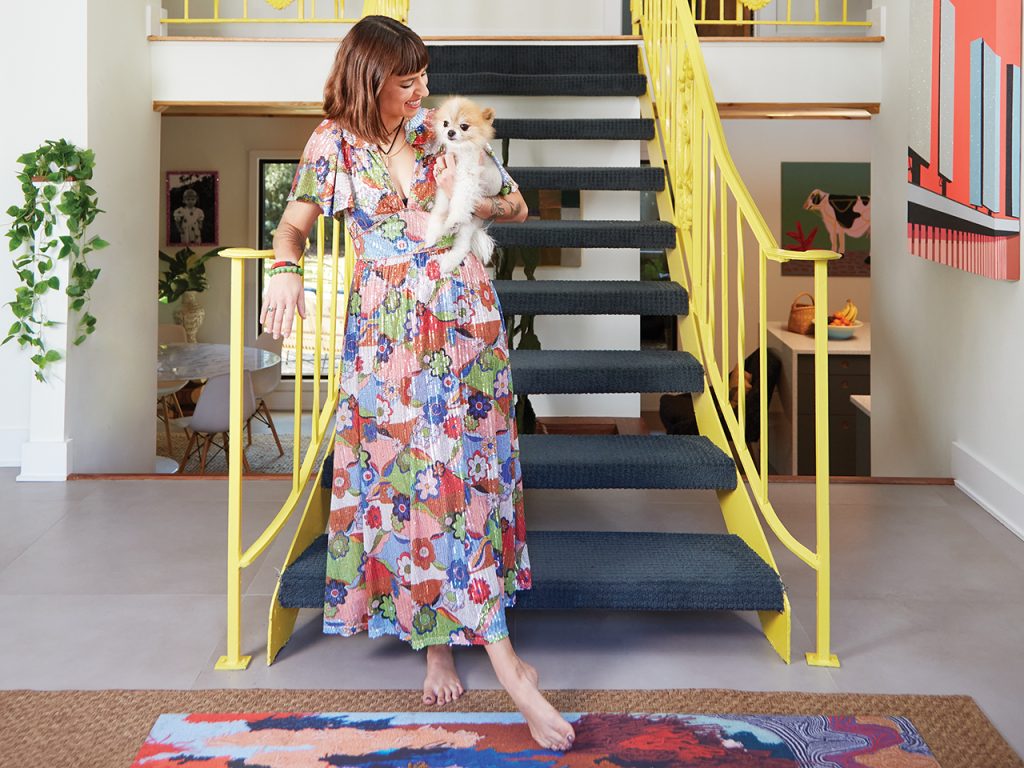 woman standing in front of a bright yellow staircase and holding a Pomeranian