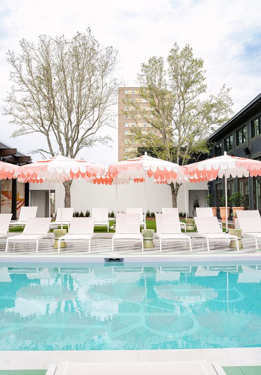 White pool chairs lined up at the edge of an in-ground pool and covered by open white-and-pink umbrellas