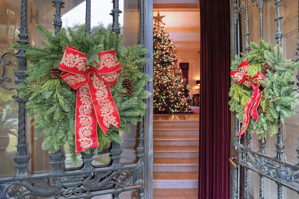 Partially opened front doors decorated with wreaths with Christmas tree in background