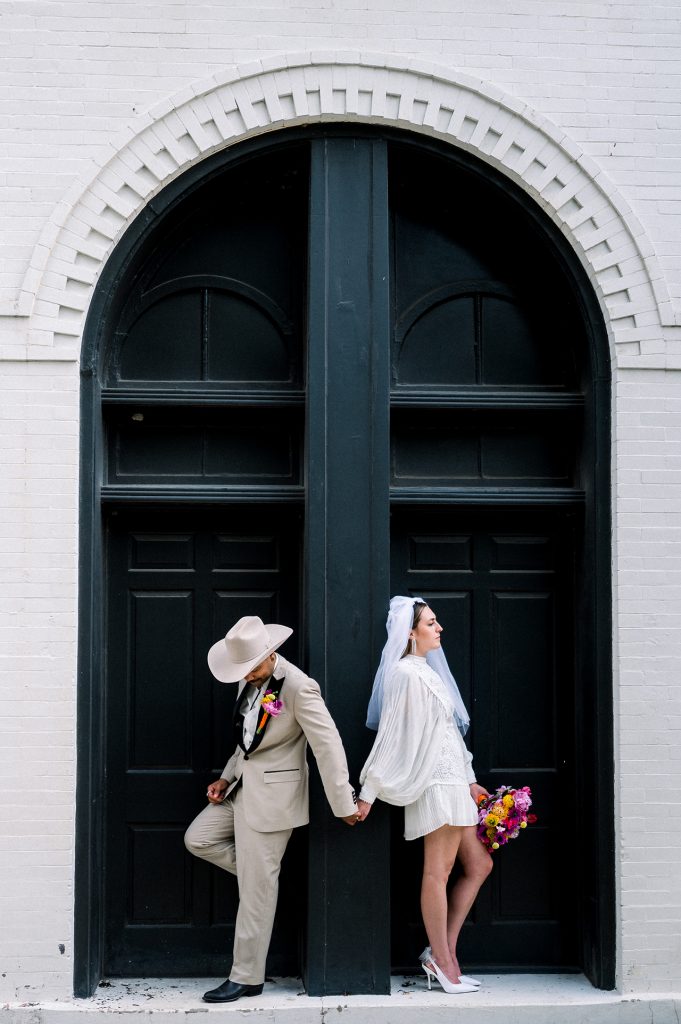 Bride and groom standing in an arched doorway holding hands