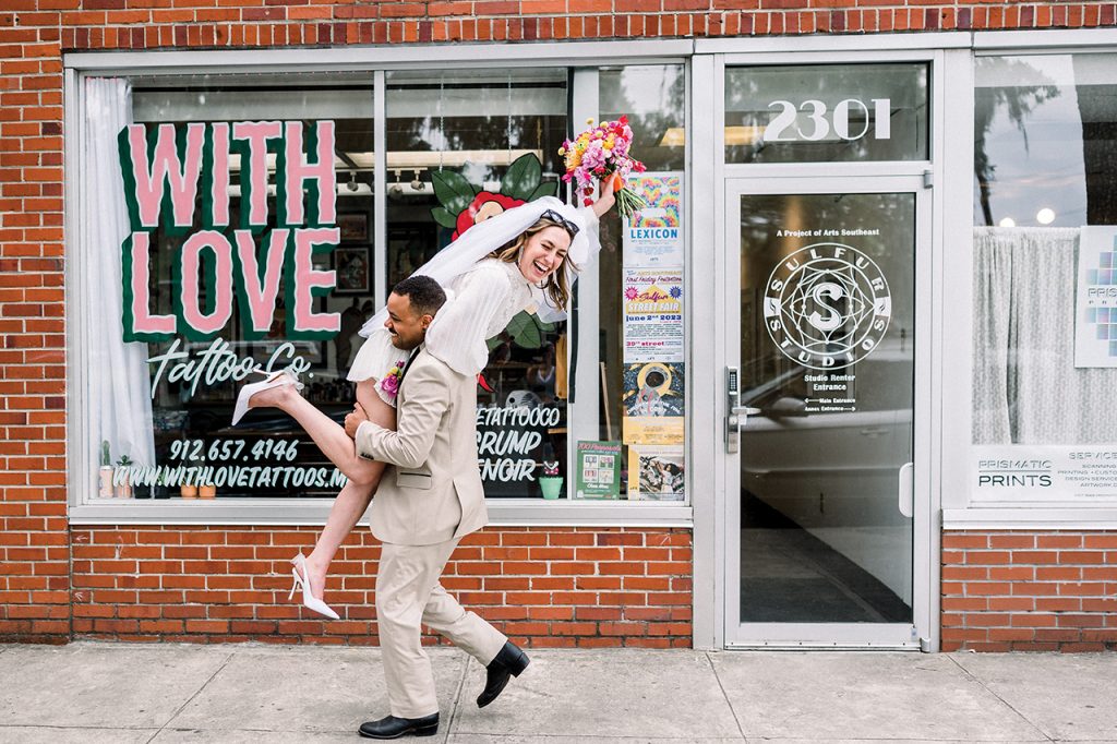 groom carrying his bride over his shoulder in front of a tattoo shop