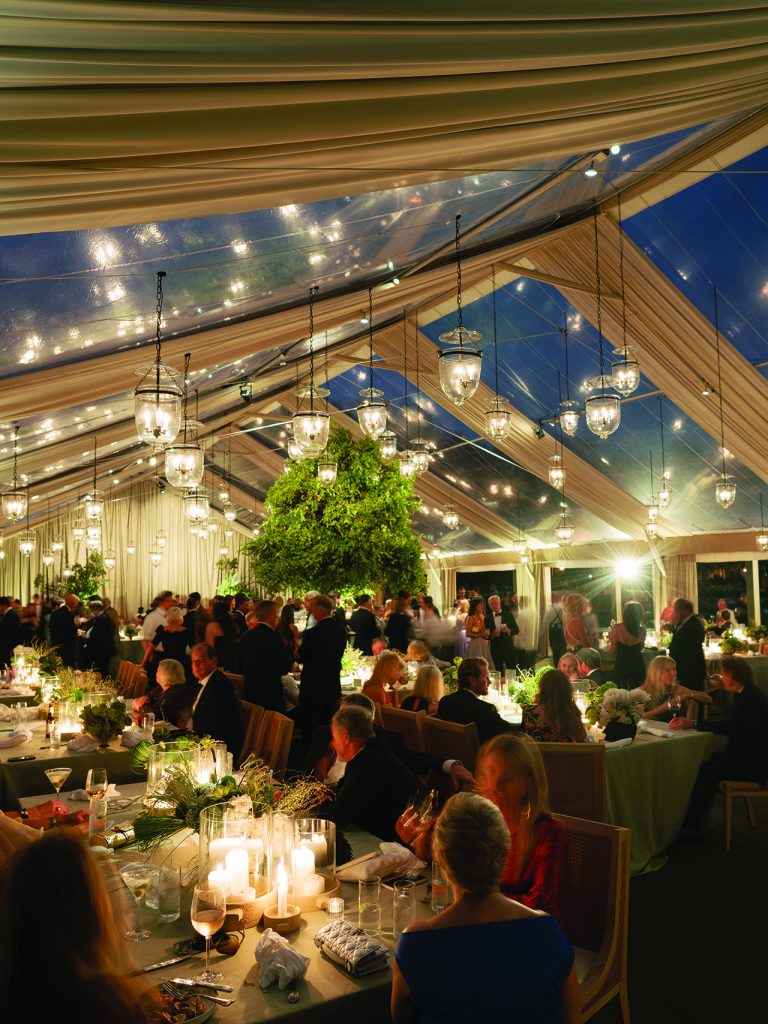 wedding reception tent with glowing lights and guests seated at long tables