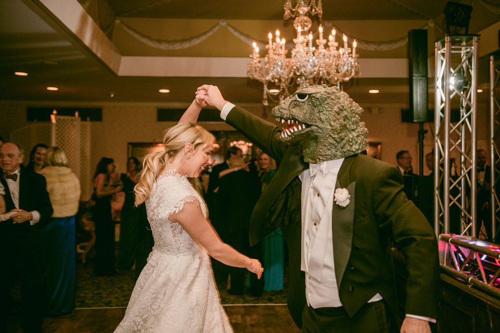 bride dancing with a man wearing a tuxedo and a Godzilla mask