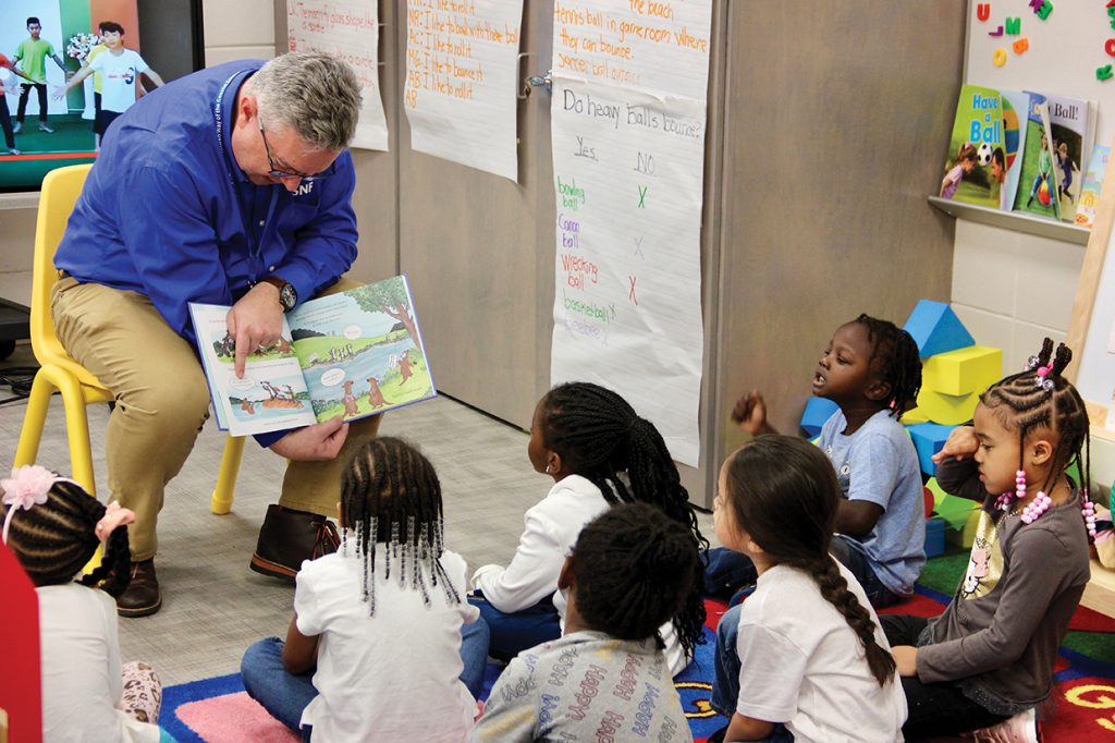 Male teacher reading a book to young students